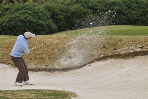 person in white shirt and brown pants holding golf club during daytime