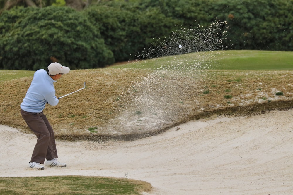 person in white shirt and brown pants holding golf club during daytime