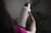 A person is holding a large, white water bottle with a metal cap. The word 'Alliance' is printed vertically on the bottle. The background is filled with green plant leaves, creating a natural setting. The person appears to be wearing a pink garment, and the lighting is dim, giving a soft and calm atmosphere.
