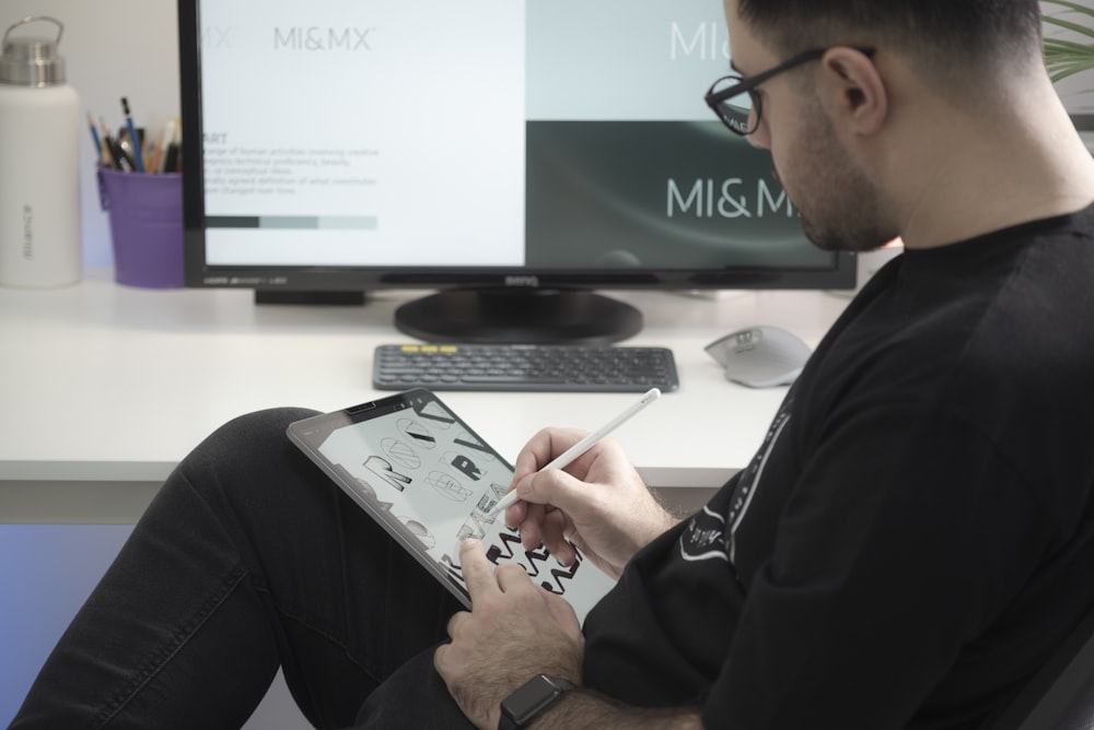 homem na camisa preta de manga comprida sentado ao lado do monitor de computador de tela plana preta