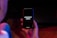 A hand is holding a black smartphone with the screen displaying the text 'OPPORTUNITY KNOCKS' in white font. The phone is surrounded by a dimly lit environment with hints of red and blue lighting.