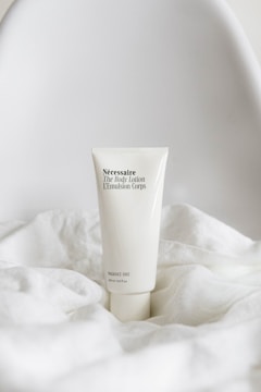 A sleek, minimalist tube of body lotion with black text is displayed elegantly on soft, white fabric, conveying a sense of purity and simplicity.