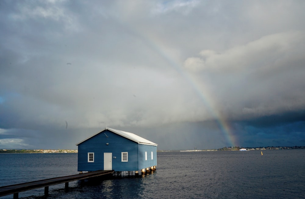 Maison en bois brun sur plan d’eau sous des nuages blancs pendant la journée