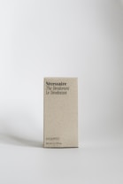A minimalist-style carton box with typography displaying the words N&eacute;cessaire The Deodorant Le D&eacute;odorant. The text is printed in black against a light beige background. It indicates the eucalyptus scent and a size of 50 ml / 1.7 fl oz. The box stands upright on a flat, light surface with a soft shadow cast beside it.