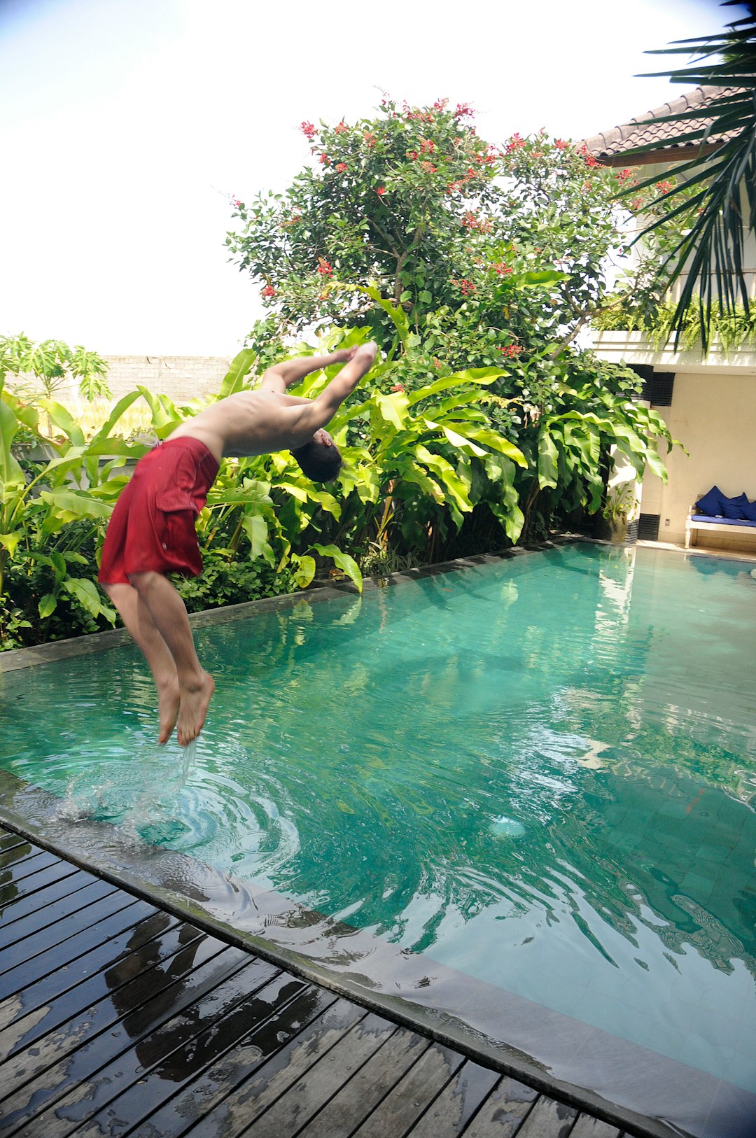 man in red shorts jumping on pool during daytime