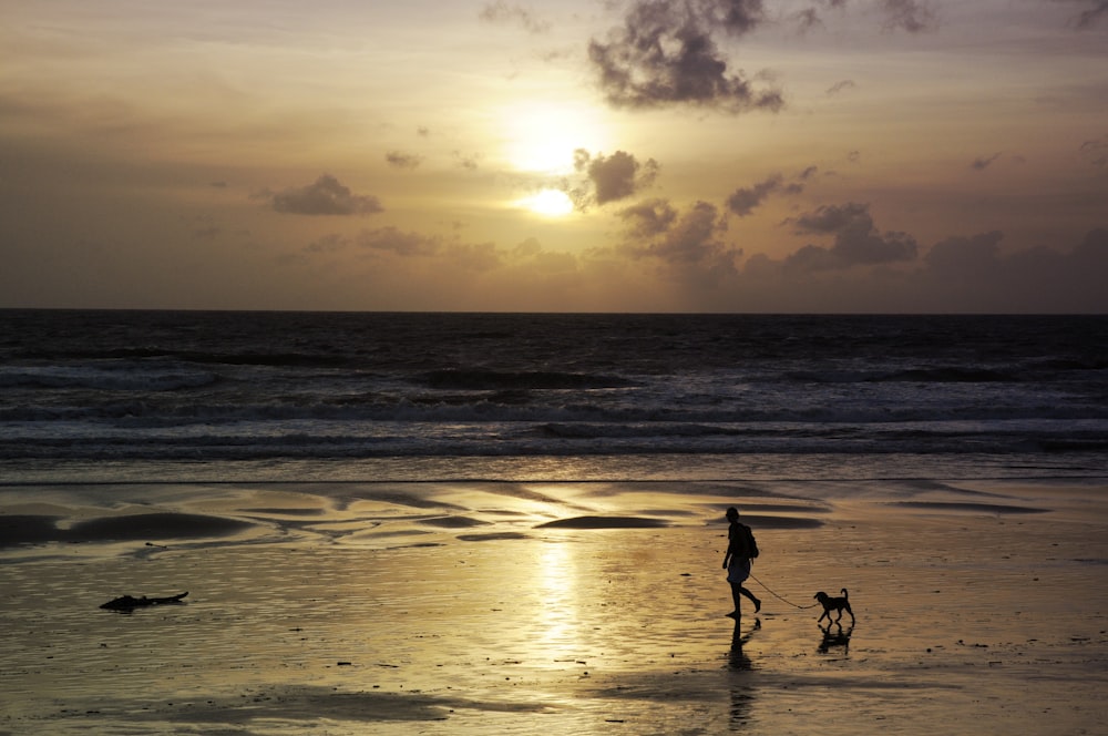 Silhouette von 2 Personen, die während des Sonnenuntergangs am Strand spazieren gehen