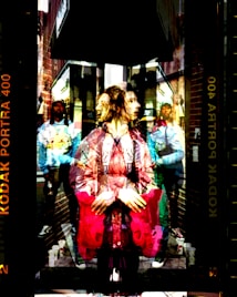 A double exposure image depicting a person with a contemplative expression in the foreground, layered over a street scene. Buildings and urban elements are visible, with people in casual attire walking in the background. The colors are vivid, creating a surreal and dynamic effect.