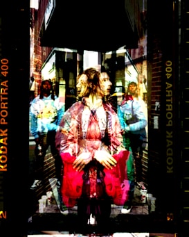 A double exposure image depicting a person with a contemplative expression in the foreground, layered over a street scene. Buildings and urban elements are visible, with people in casual attire walking in the background. The colors are vivid, creating a surreal and dynamic effect.