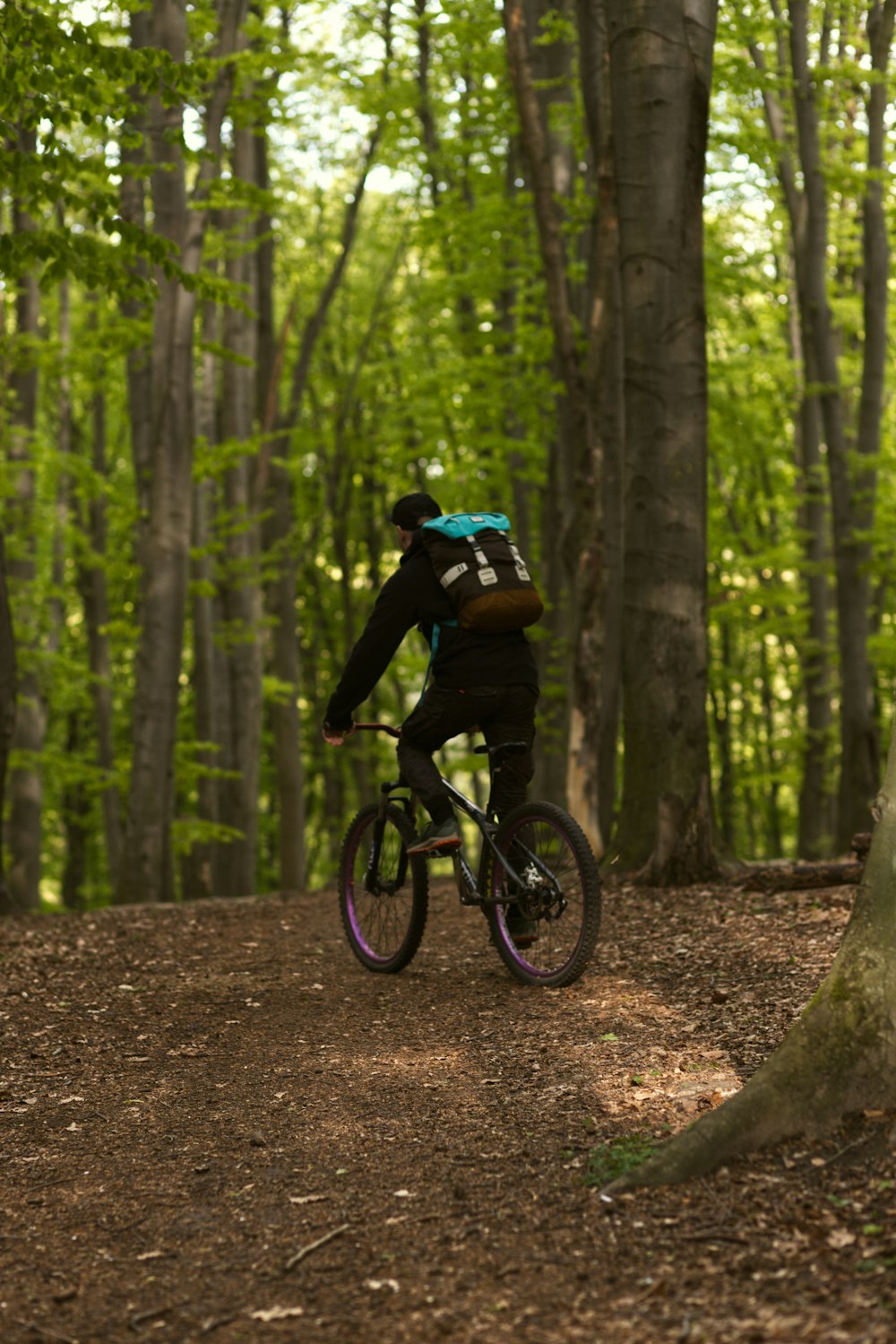 검은 재킷을 입은 남자가 낮에 숲에서 자전거를 타고 있습니다.