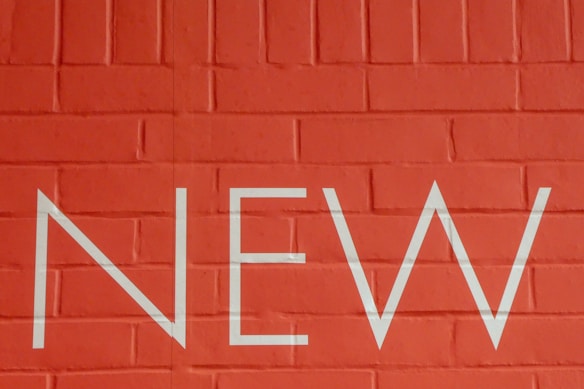 A red brick wall with the word 'NEW' printed in large white letters across the center.
