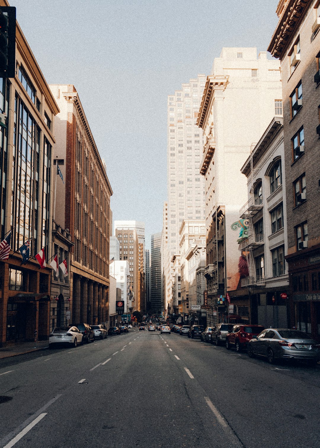 cars parked on side of the road in between high rise buildings during daytime