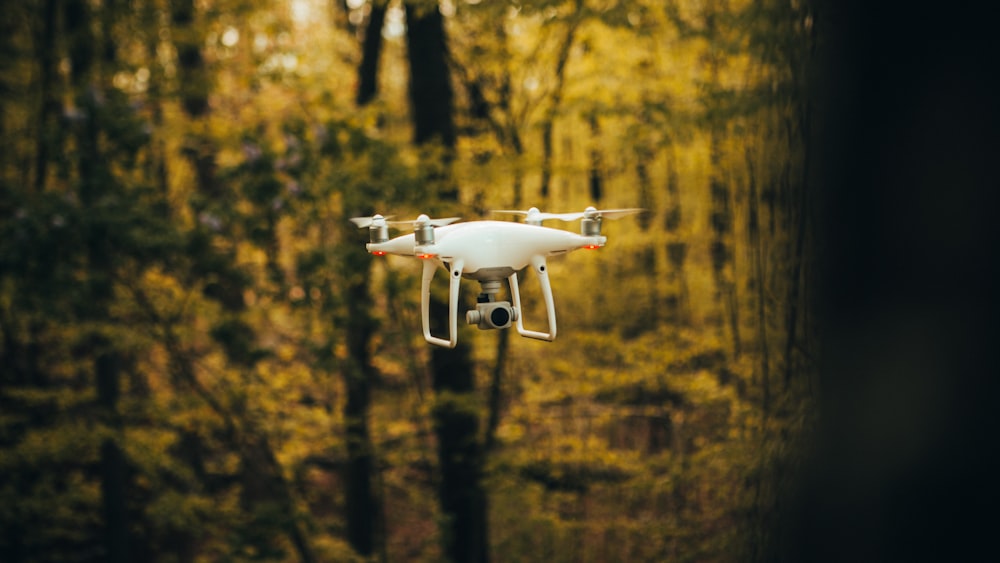 white drone flying over the forest during daytime
