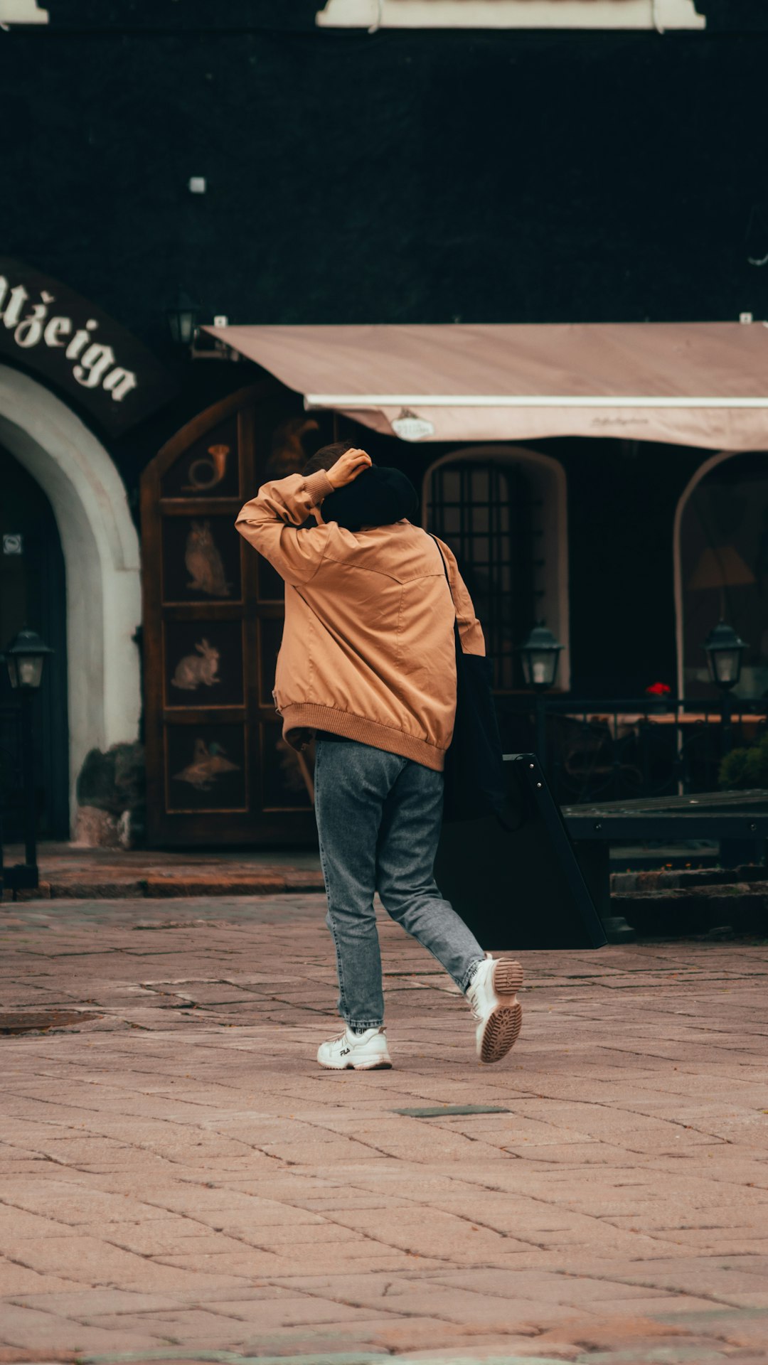 man in brown hoodie and blue denim jeans standing on sidewalk during daytime
