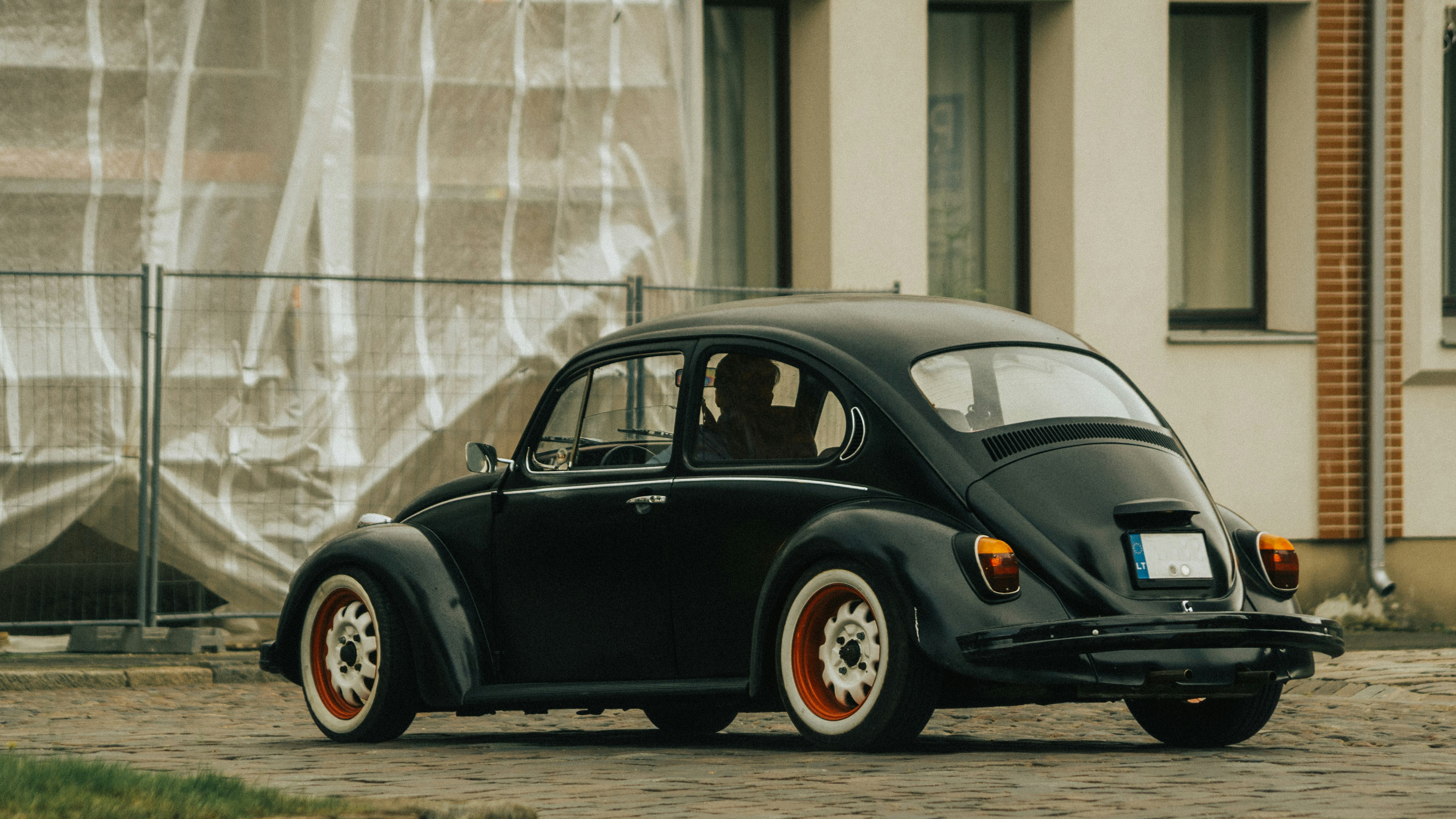 black volkswagen beetle parked beside white wall