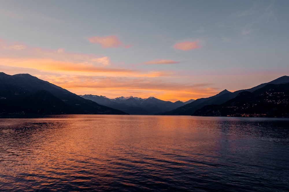 silhouette of mountain near body of water during sunset