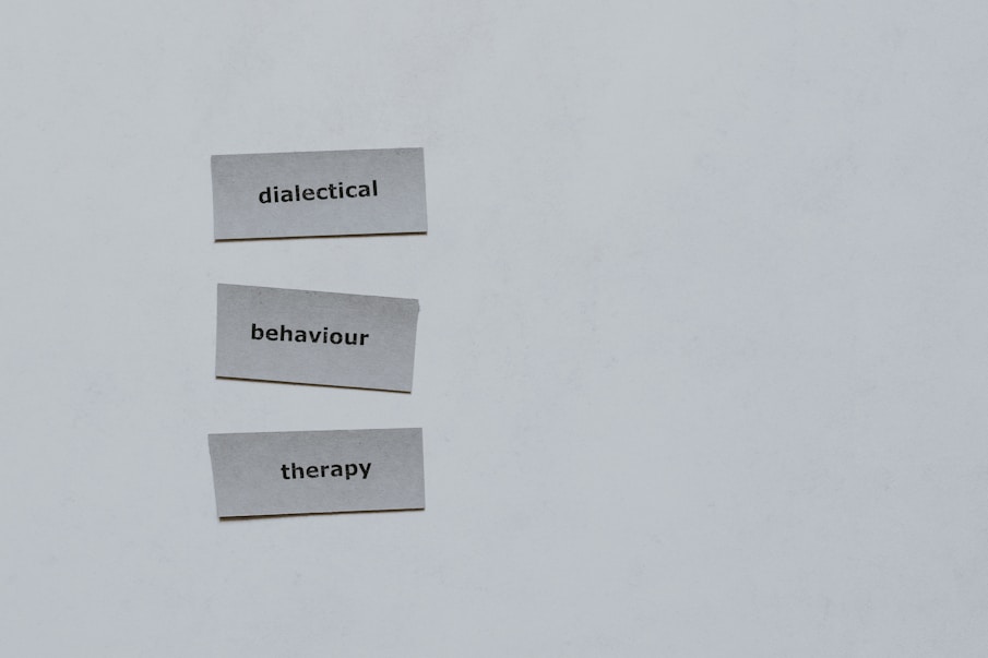 Three pieces of paper arranged vertically feature the words 'dialectical', 'behaviour', and 'therapy'. The background is a plain light gray.