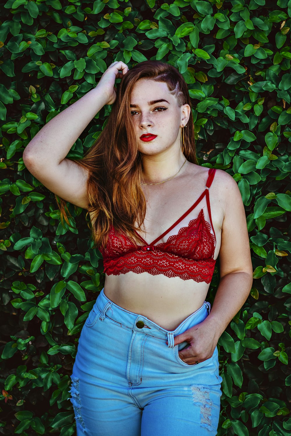 woman in red brassiere and blue denim shorts standing beside green plants