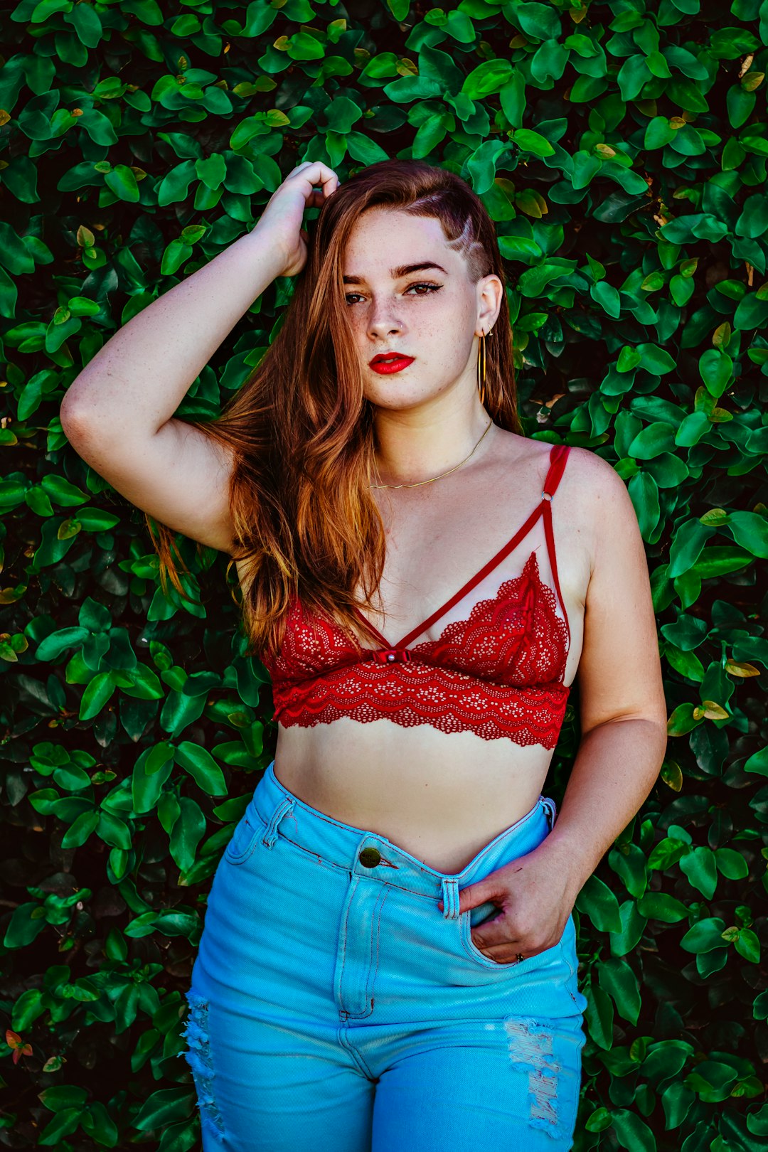 woman in red brassiere and blue denim shorts standing beside green plants