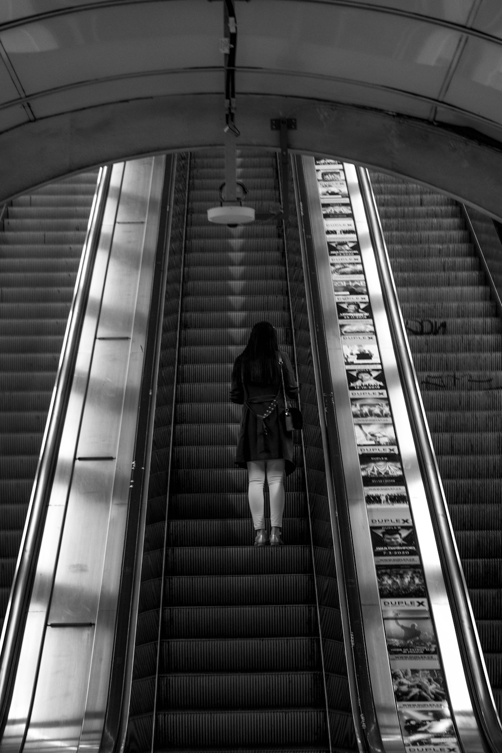 grayscale photo of woman walking on escalator