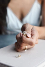 Close-up of a hand wearing layered delicate gold rings against a soft pastel background.