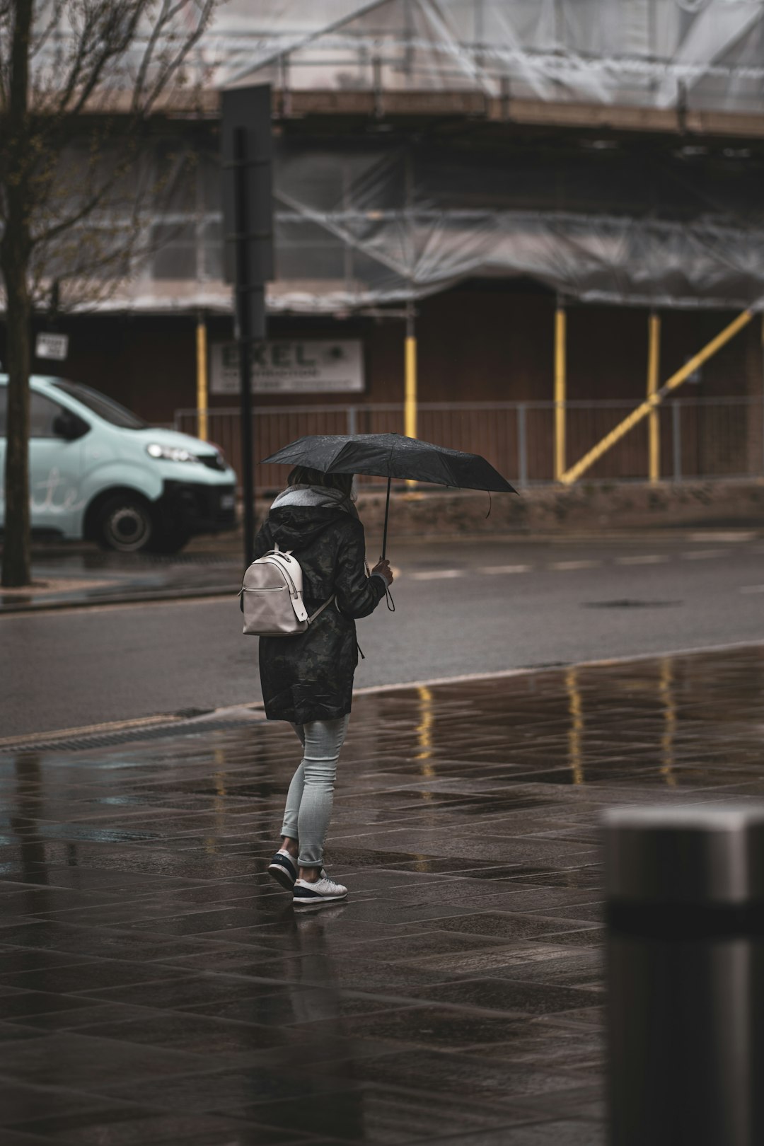 person in black jacket and black pants holding umbrella walking on sidewalk during daytime