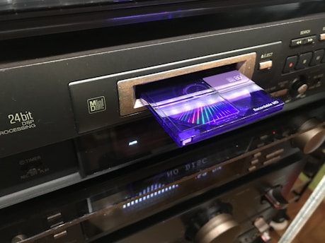 A close-up of a vintage Minidisc player with a glowing display, set against a cozy wooden desk background.