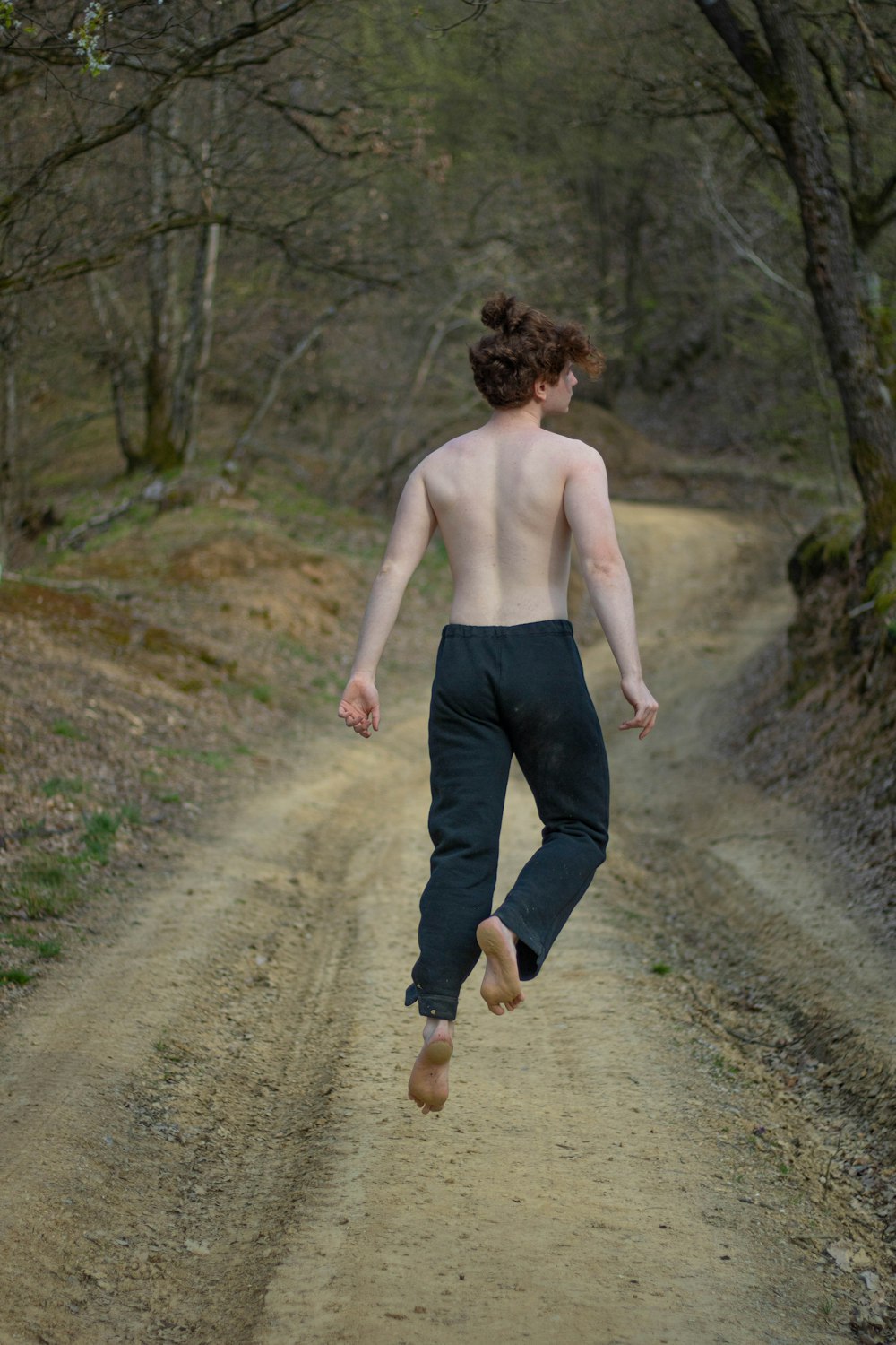 topless man in black pants walking on dirt road during daytime