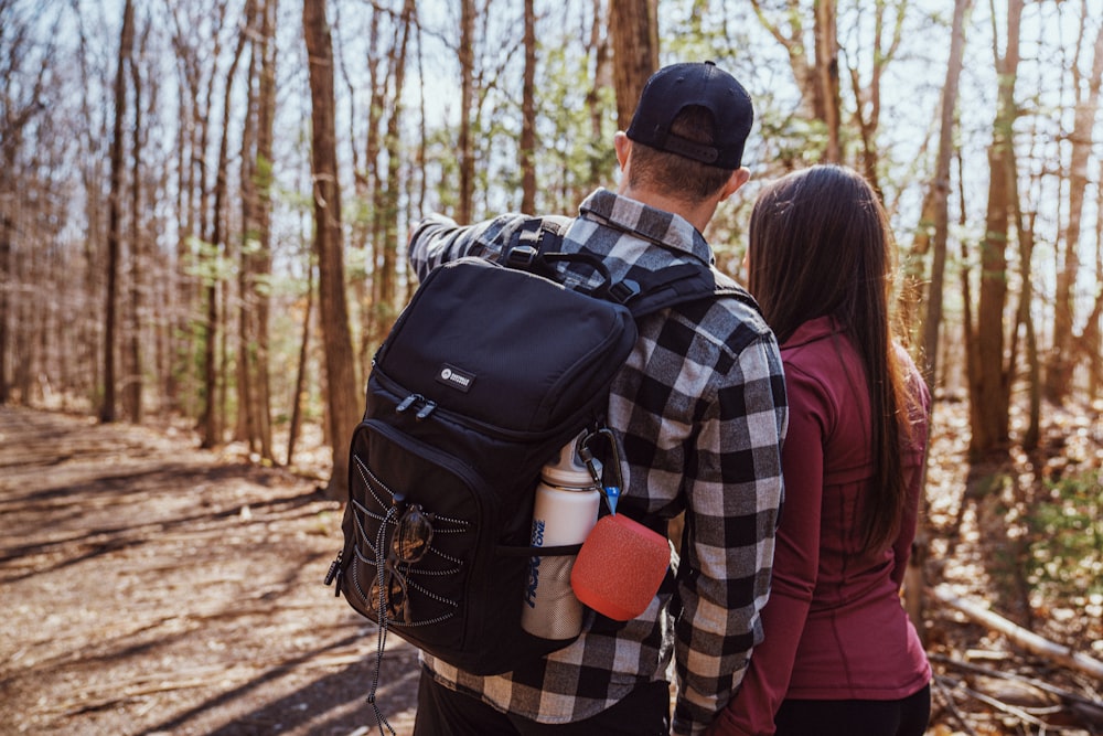 man and woman wearing black and blue backpacks standing on brown dirt road during daytime