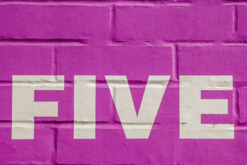 uma parede de tijolos cor-de-rosa com a palavra cinco pintada nela