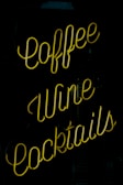 A neon sign featuring the words 'coffee', 'wine', and 'cocktails', with bright yellow lettering against a dark background.