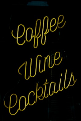 A neon sign featuring the words 'coffee', 'wine', and 'cocktails', with bright yellow lettering against a dark background.
