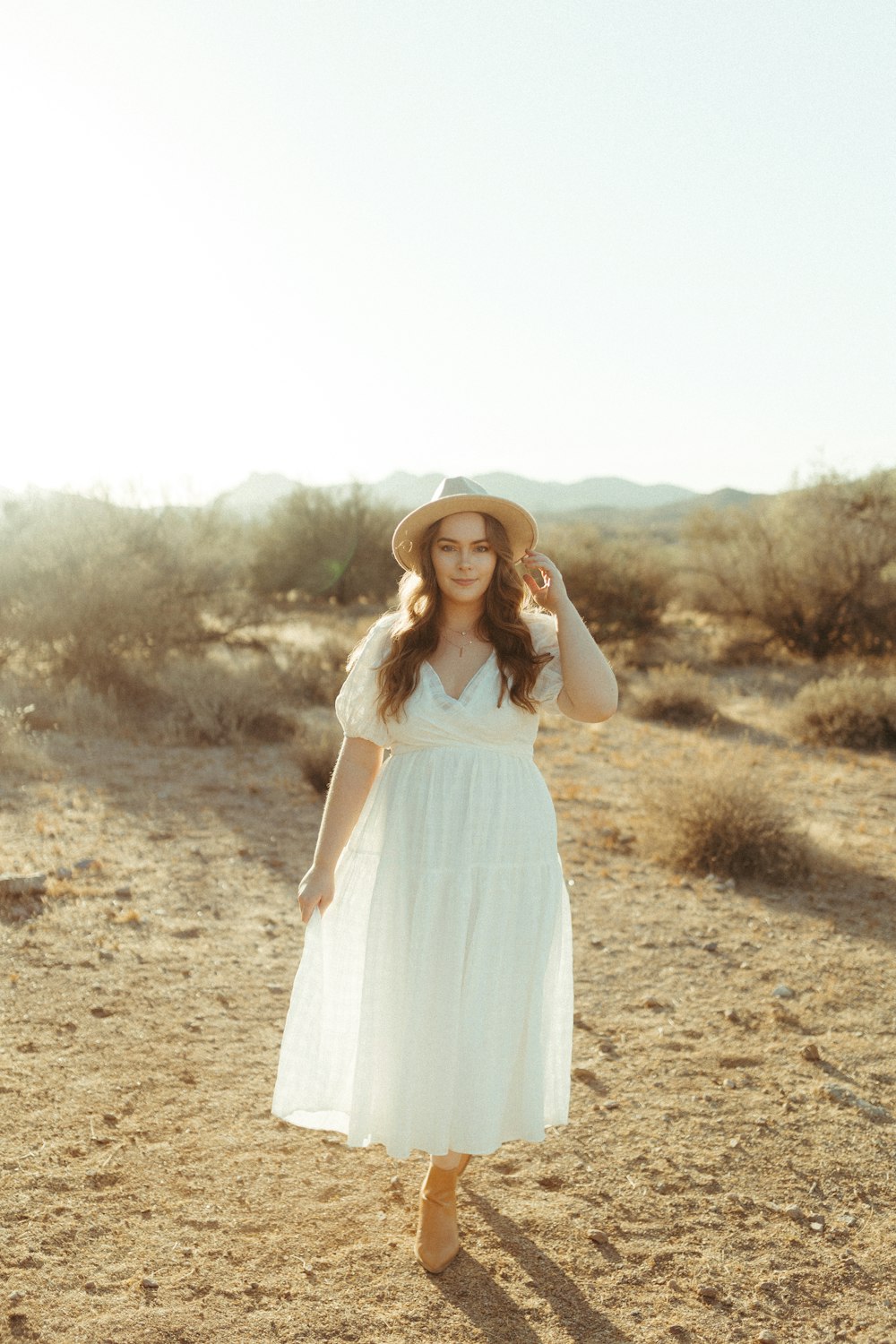 donna in abito bianco in piedi su campo marrone durante il giorno