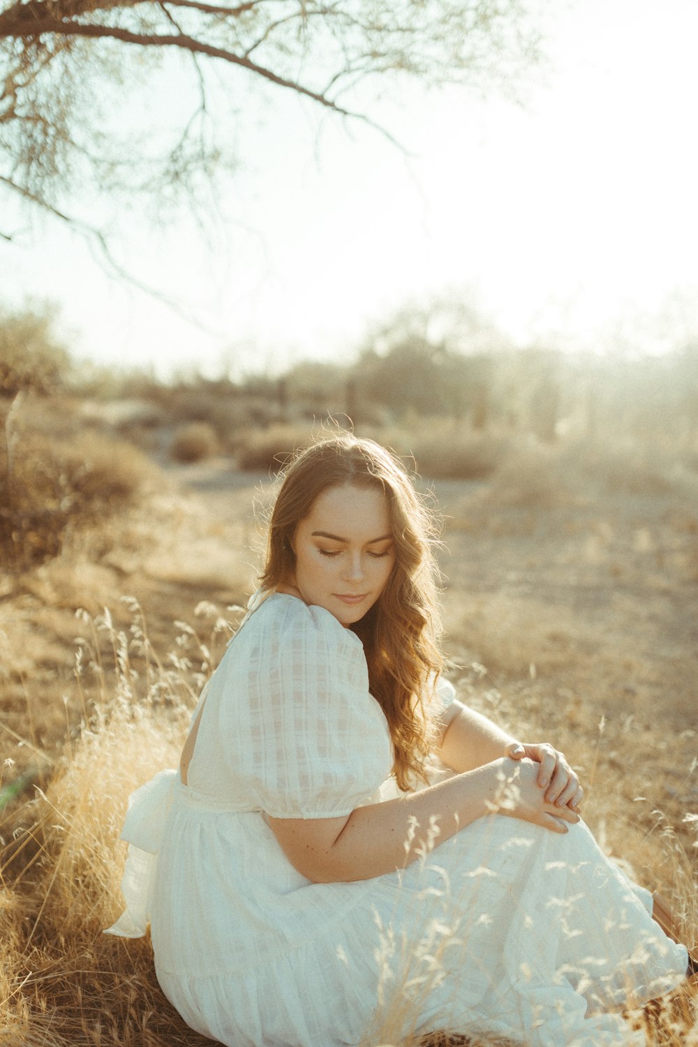 woman in white and blue plaid dress shirt sitting on brown grass field during daytime