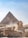A large pyramid and the Great Sphinx against a backdrop of a clear sky. Several tourists are present, walking along designated paths.