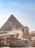 A large pyramid and the Great Sphinx against a backdrop of a clear sky. Several tourists are present, walking along designated paths.