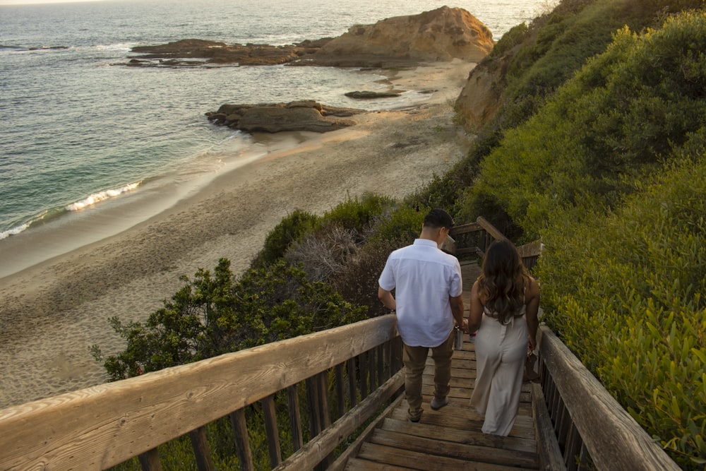 man and woman walking on wooden bridge near body of water during daytime