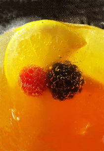 A close-up of a sparkling citrus-flavored Brightside drink surrounded by fresh lemon and herbs.