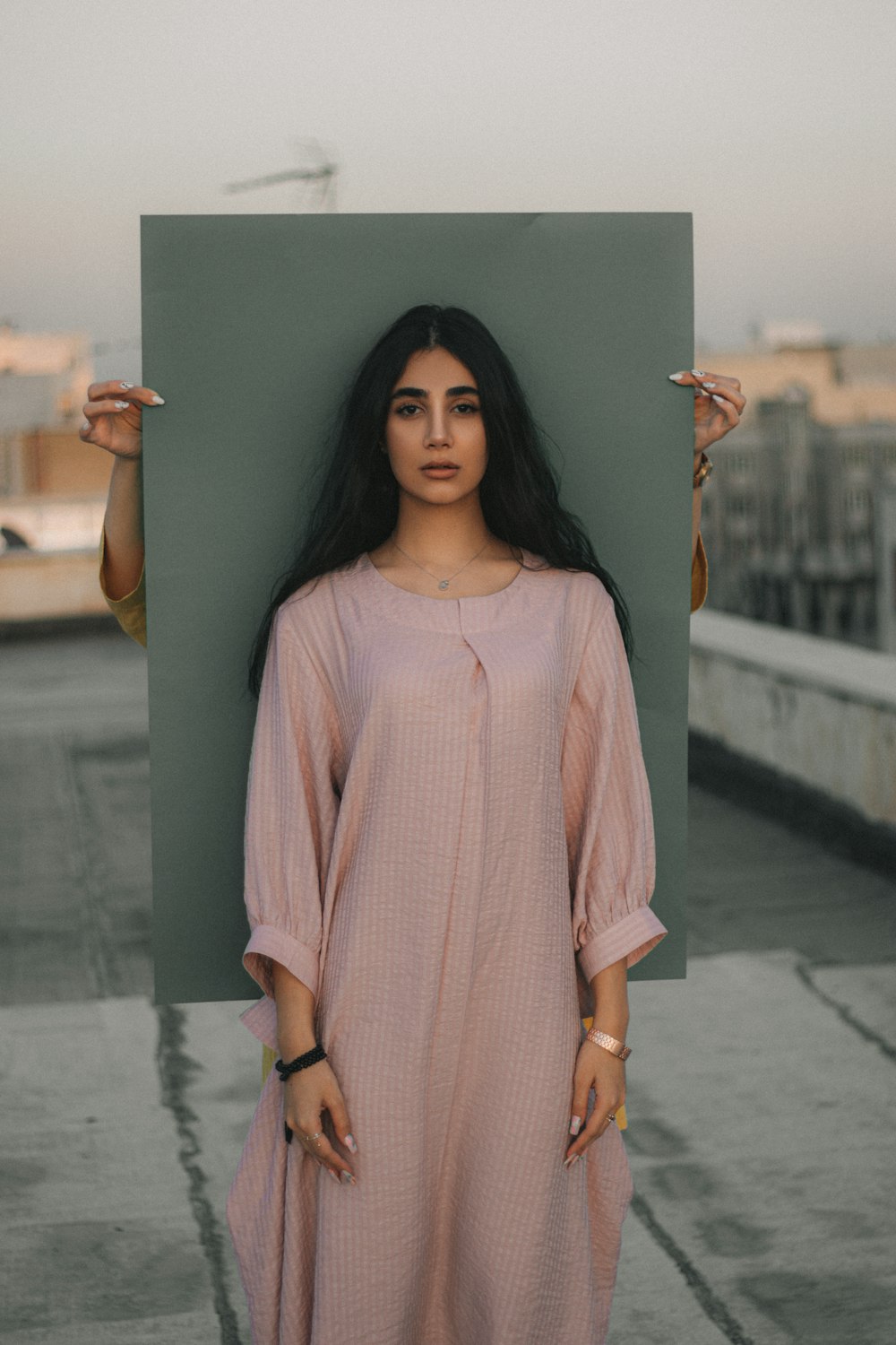 Mujer en vestido de lunares rosa y blanco de pie junto a la pared de hormigón gris durante el día