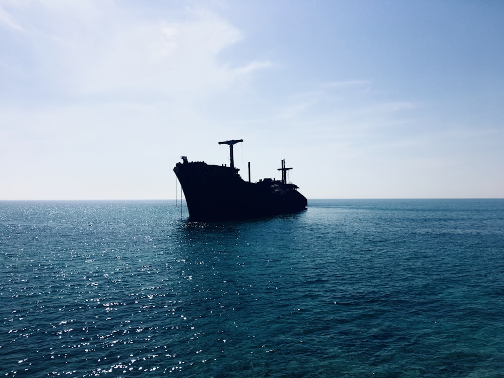 昼間の白い空の下、海に浮かぶ黒い船