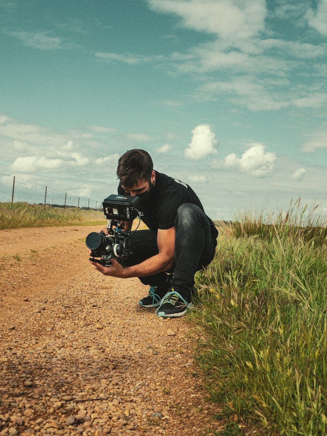 man in black t-shirt and black shorts sitting on brown field holding black dslr camera