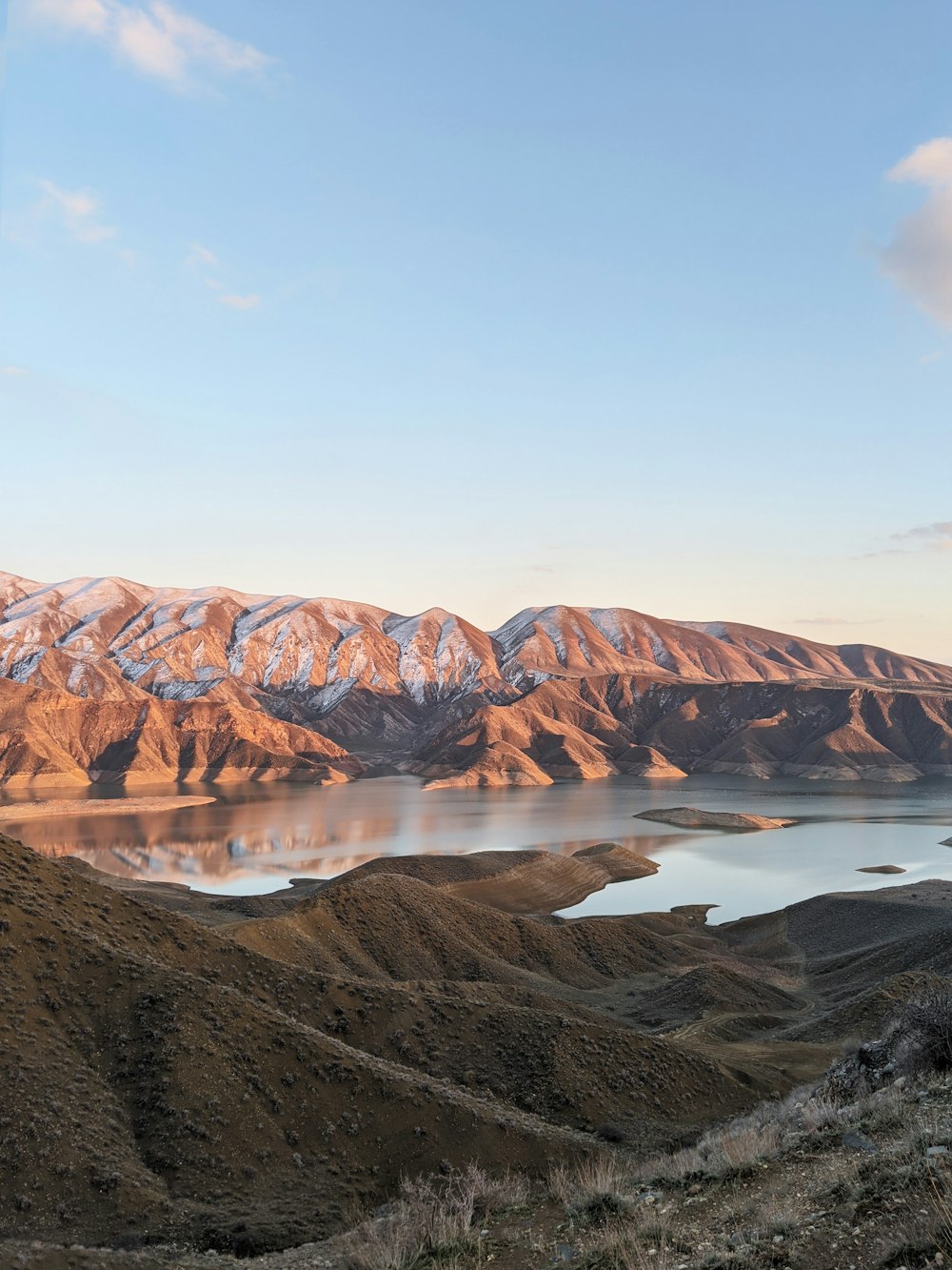 Montaña marrón cerca del lago bajo el cielo azul durante el día