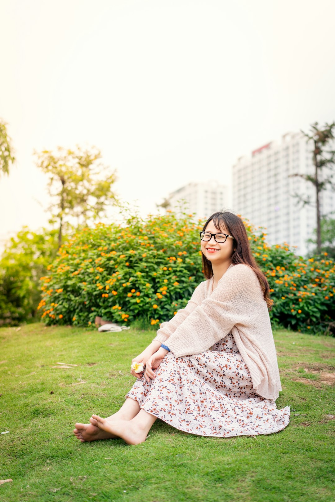 woman in gray cardigan and black and white floral dress sitting on green grass field during