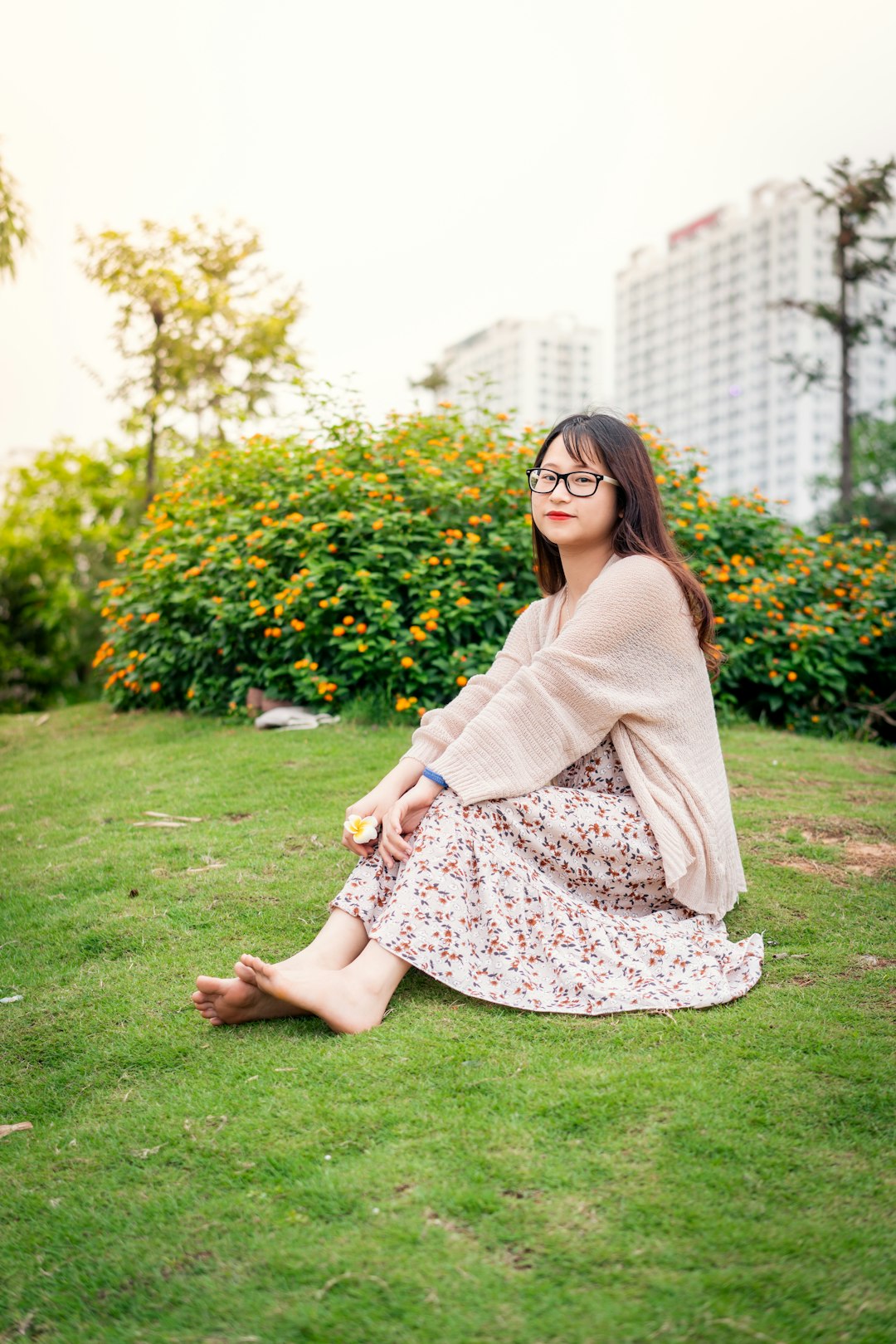 woman in gray long sleeve shirt and pink floral skirt sitting on green grass field during