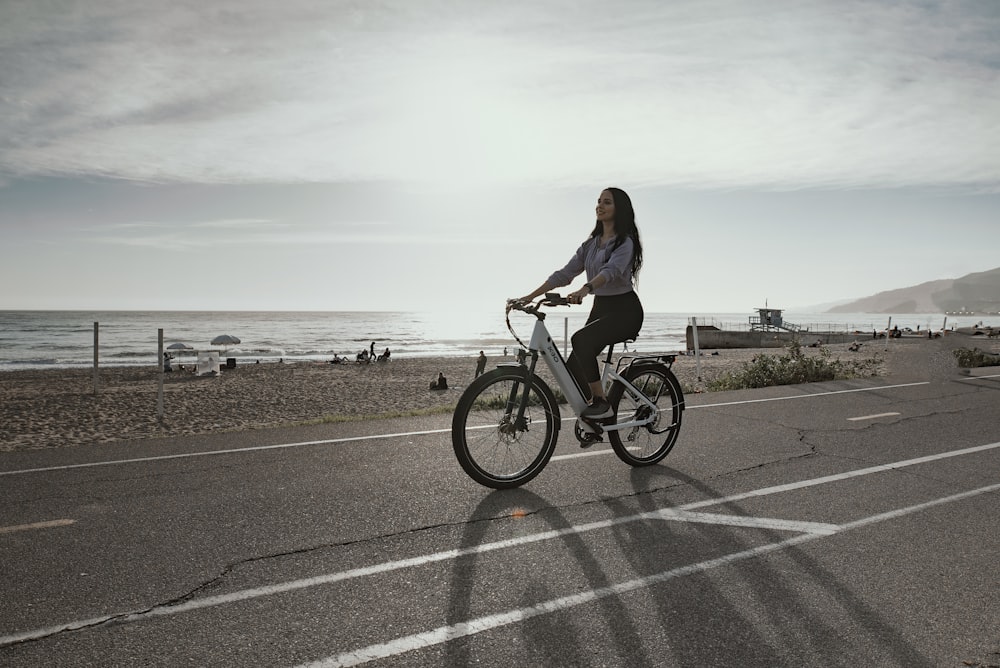 Donna in camicia nera a maniche lunghe in sella alla bicicletta sulla strada asfaltata grigia durante il giorno