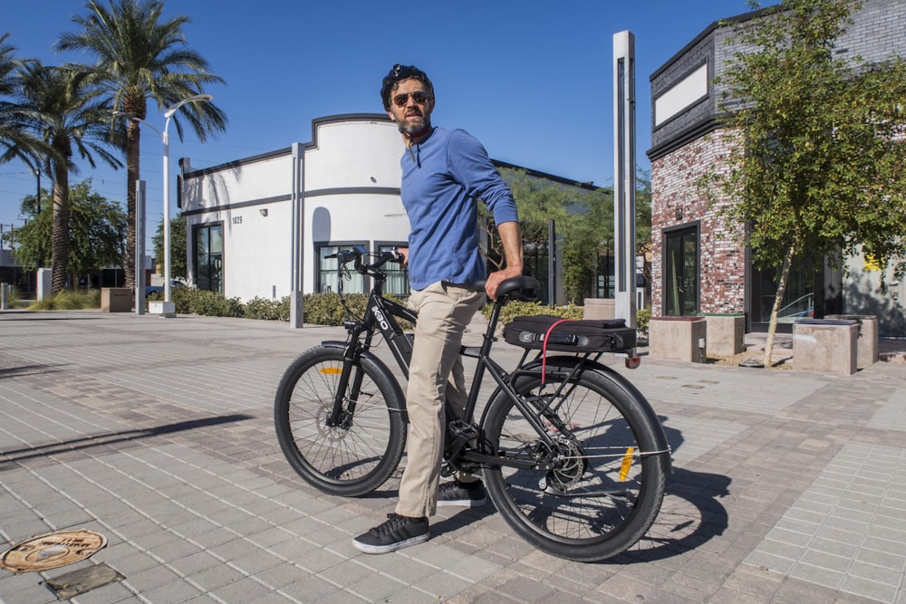 man in blue dress shirt and brown pants riding on black bicycle during daytime