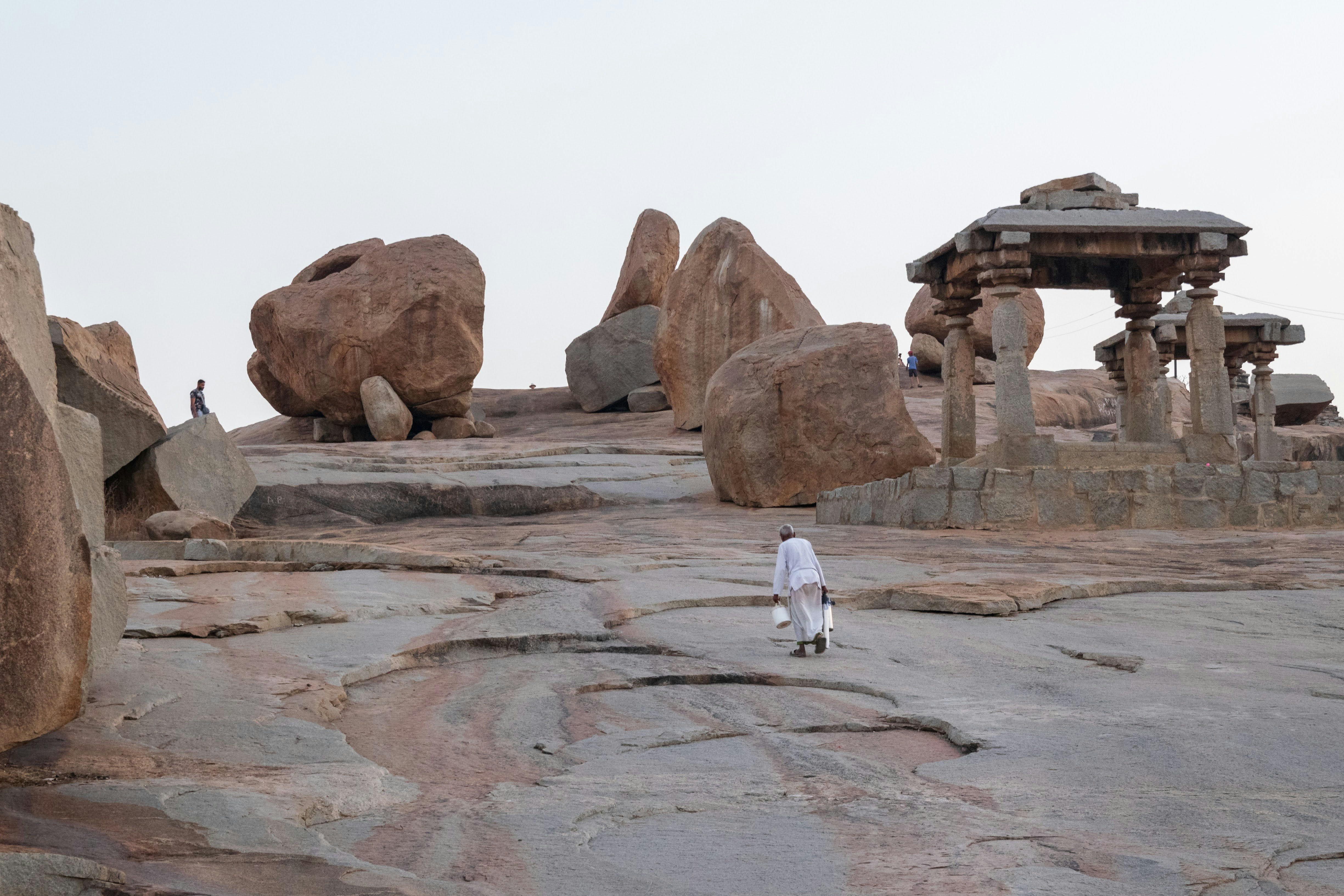 person in white robe walking on brown rock formation during daytime, Hemakuta Hill inclination, Hampi, Karnataka
