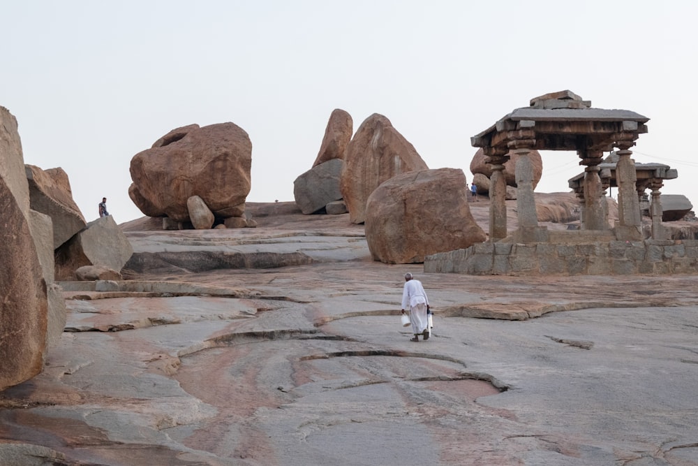 Persona con túnica blanca caminando sobre la formación rocosa marrón durante el día
