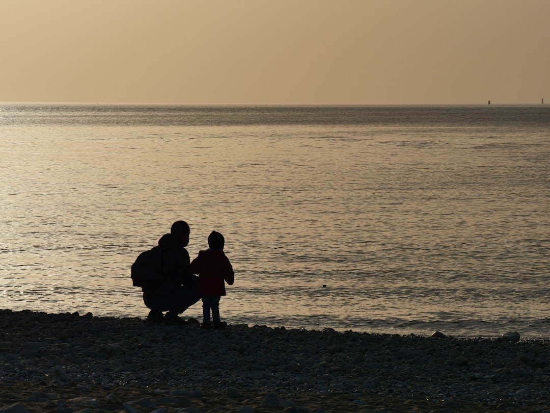 silhouette of 3 people sitting on seashore during sunset