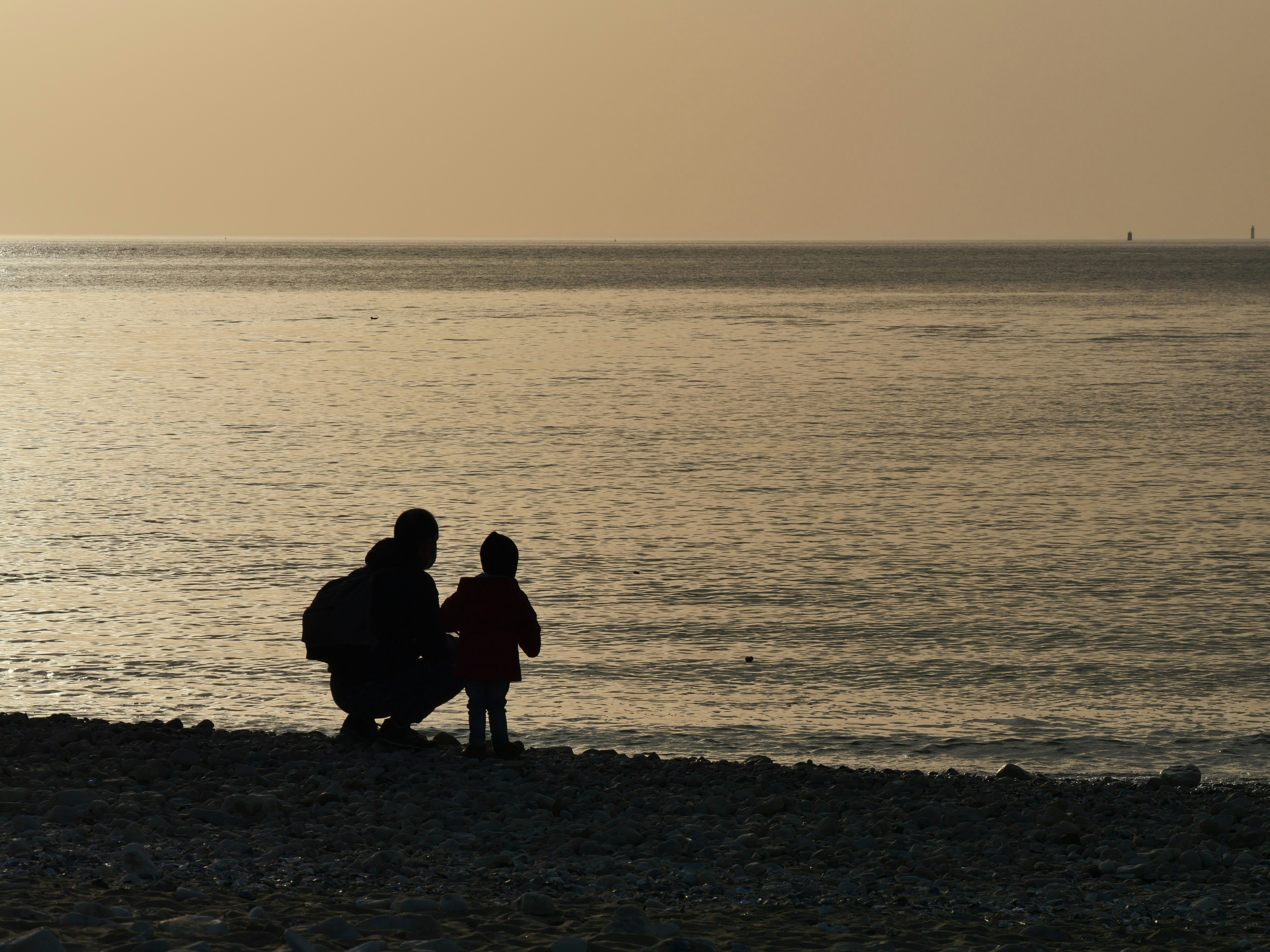 silhouette of 3 people sitting on seashore during sunset