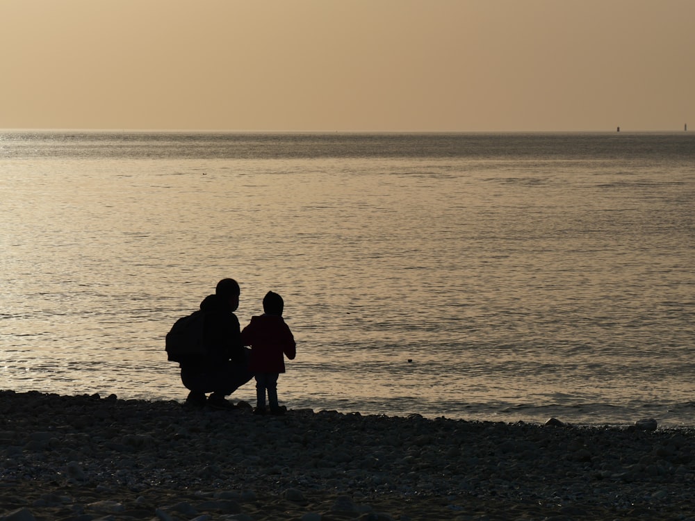 silhouette of 3 people sitting on seashore during sunset